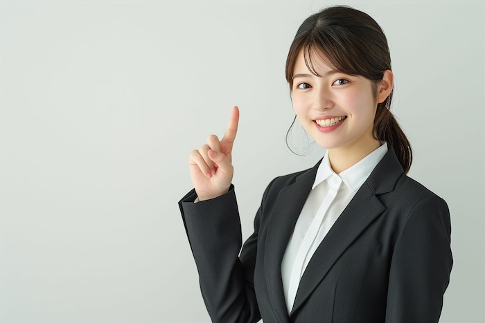 指をさす日本人の女性ビジネスマンウーマンのポートレート写真(白背景・会社員・スーツ・若手・OL・新入社員・窓口・案内)